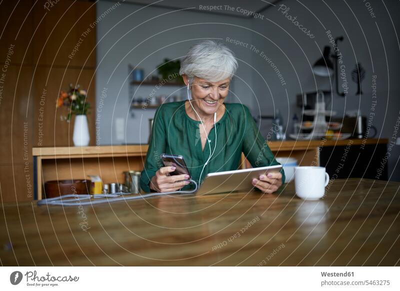 Senior woman listening to music while using smart phone and digital tablet at home color image colour image indoors indoor shot indoor shots interior