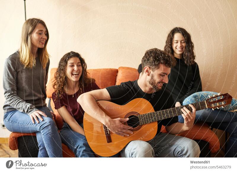 Happy freinds listening to man playing guitar on couch friends group of people Group groups of people happiness happy together settee sofa sofas couches settees