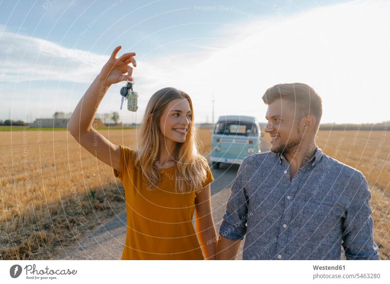 Young couple with car key on dirt track at camper van in rural landscape keys happiness happy country countryside landscapes scenery terrain twosomes