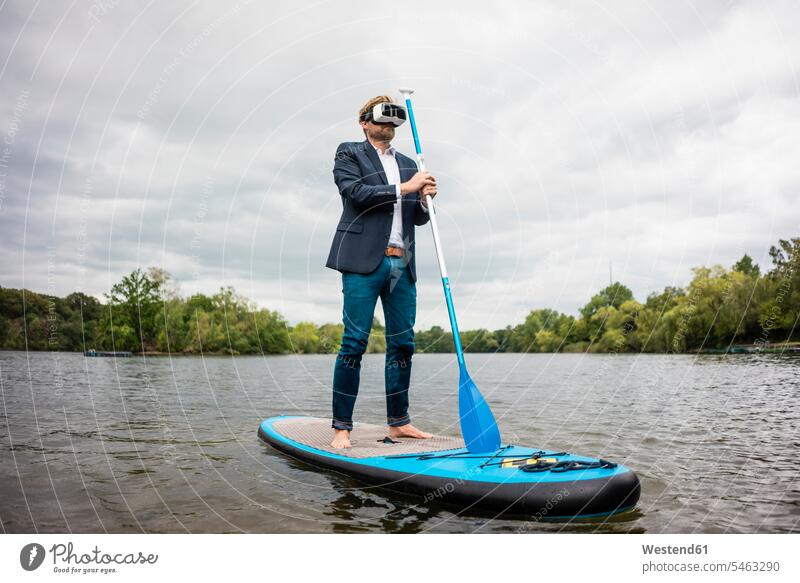 Businessman wearing VR glasses on SUP board on a lake business life business world business person businesspeople Business man Business men Businessmen