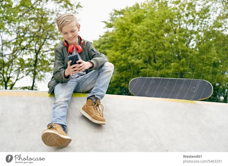 Boy with headphones in skatepark using smartphone headset Smartphone iPhone Smartphones skateboarder skater skateboarders skaters boy boys males smiling smile