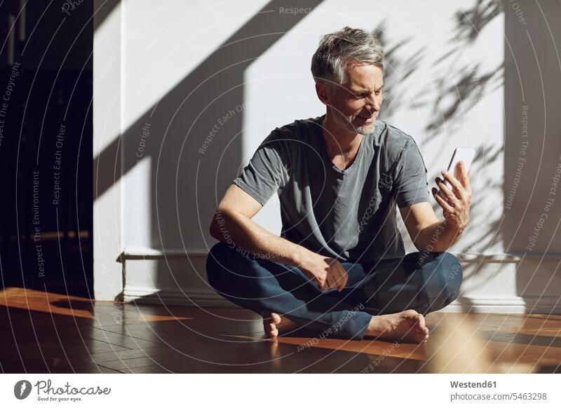 Mature man sitting on the floor at home using cell phone human human being human beings humans person persons celibate celibates singles solitary people