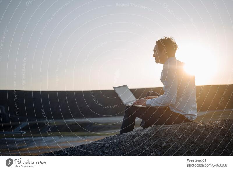 Mature businessman using laptop on a disused mine tip at sunset human human being human beings humans person persons caucasian appearance caucasian ethnicity