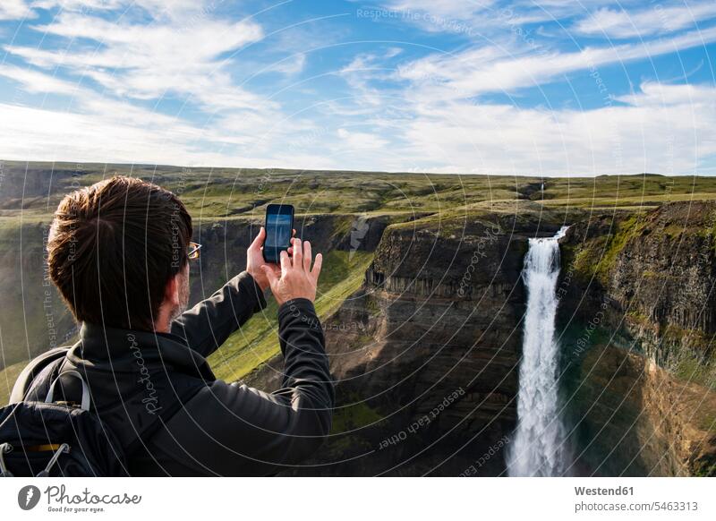 Tourist taking photo of Haifoss waterfall through mobile phone while standing at Iceland color image colour image outdoors location shots outdoor shot