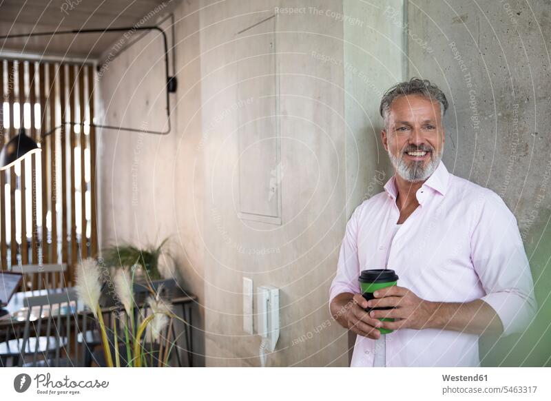 Smiling businessman holding coffee mug at concrete wall in a loft smiling smile concrete walls lofts Coffee Mug Coffee Mugs Businessman Business man Businessmen