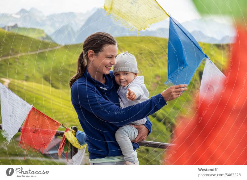 Germany, Bavaria, Oberstdorf, happy mother carrying little daughter on a mountain hut surrounded by pennants mommy mothers mummy mama streamer streamers