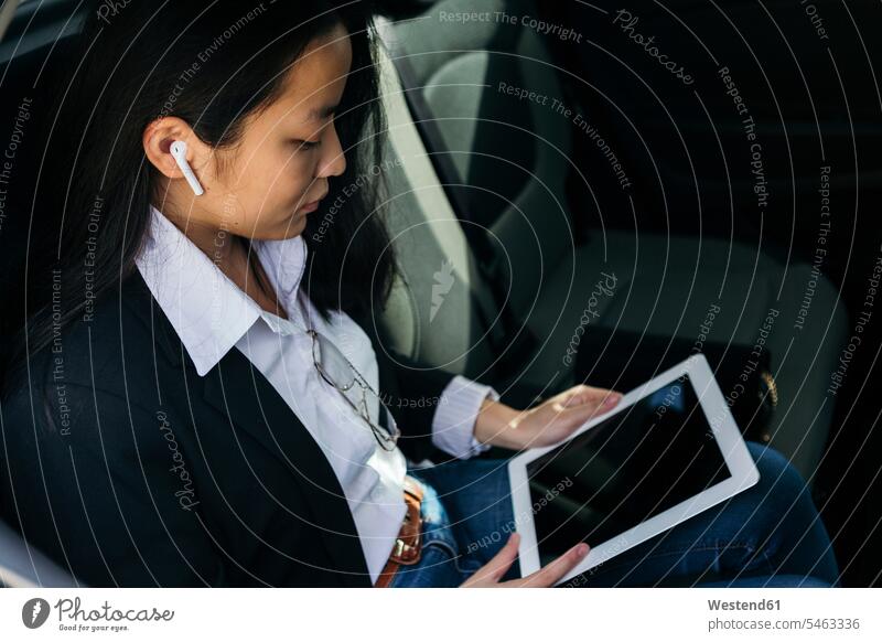 Young businesswoman sitting in car using earpods and digital tablet human human being human beings humans person persons adult grown-up grown-ups grownup