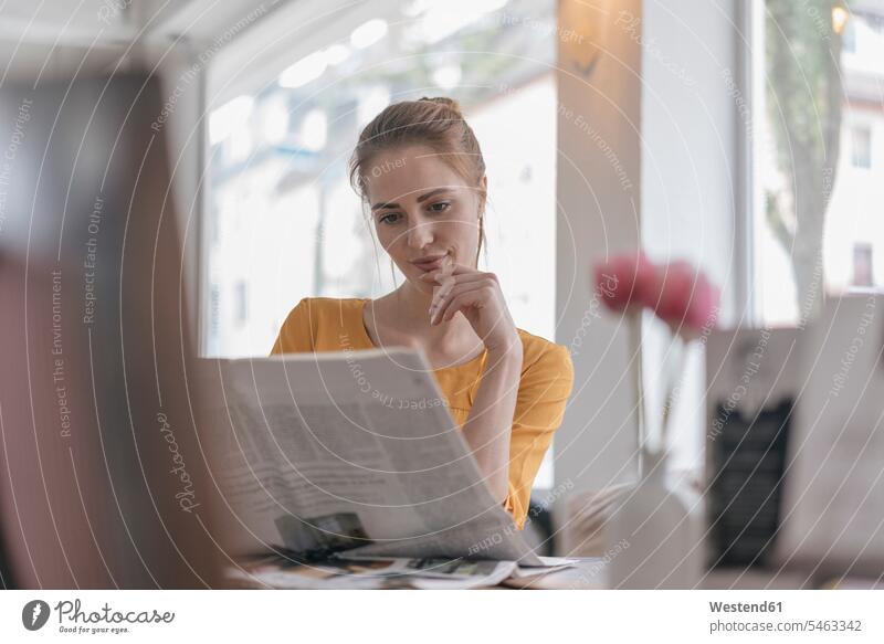 Young woman sitting in coworking space, reading newspaper cafe newspapers Seated Coworking space shared workspace office sharing females women Co-working