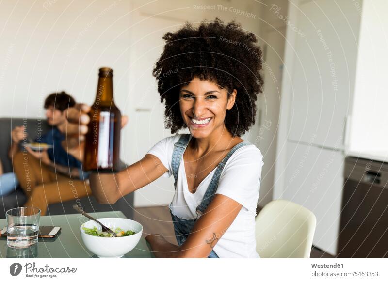 Portrait of smiling woman raising beer bottle at dining table - a ...