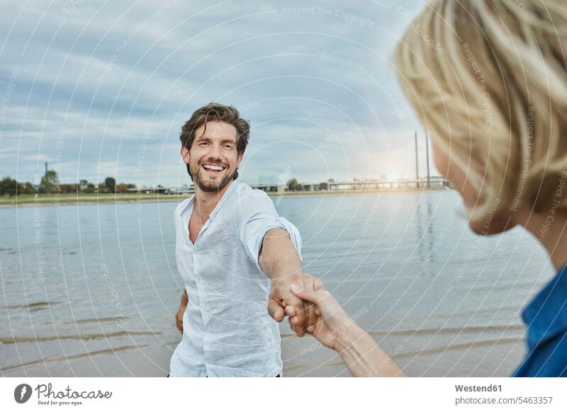 Germany, Duesseldorf, happy young couple at Rhine riverbank happiness riverside twosomes partnership couples River Rivers water's edge waterside shore people