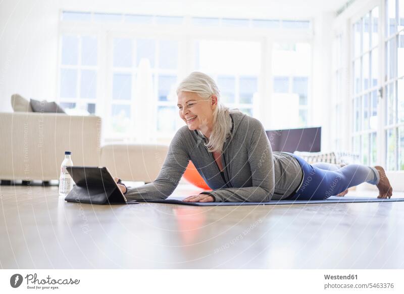 Smiling senior woman looking at digital tablet while e-learning exercises from digital tablet in apartment color image colour image Denmark Scandinavia