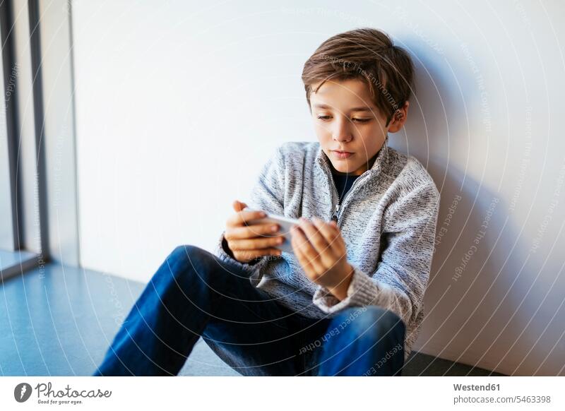 Boy sitting on floor looking at cell phone boy boys males mobile phone mobiles mobile phones Cellphone cell phones floors Seated eyeing child children kid kids