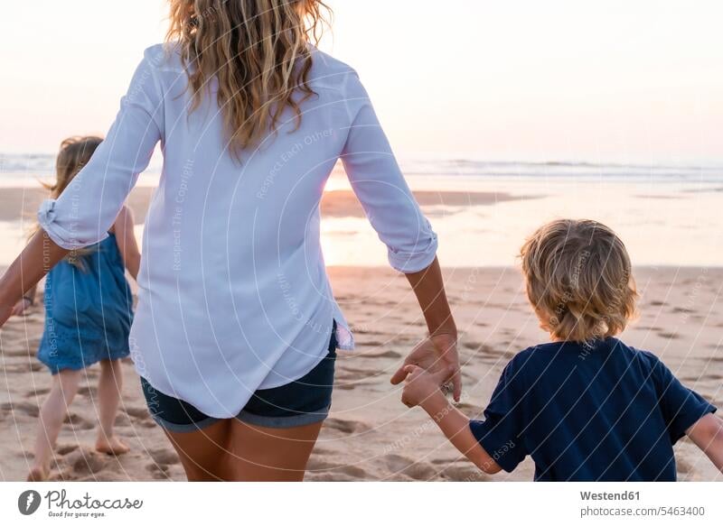 Mother with children running toward sea during sunset color image colour image outdoors location shots outdoor shot outdoor shots sunsets sundown atmosphere
