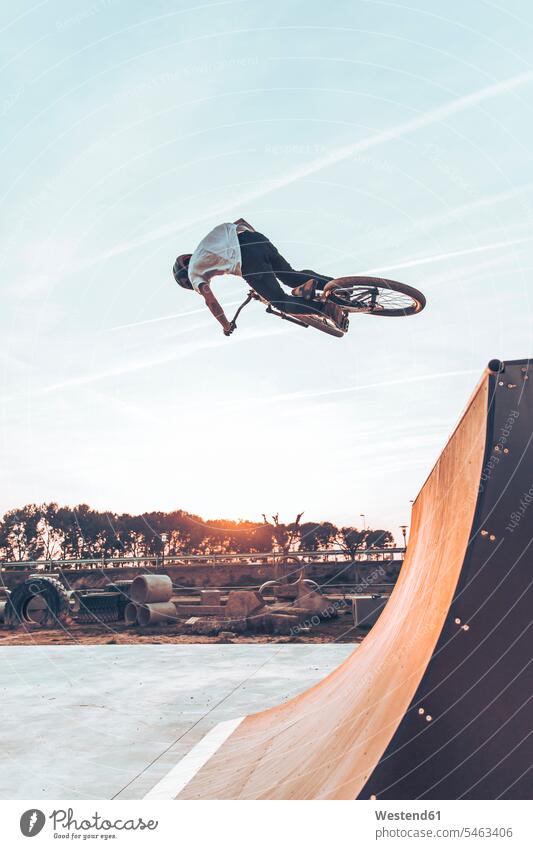 Carefree man performing stunt with bicycle on ramp against sky in park at sunset color image colour image Spain leisure activity leisure activities free time
