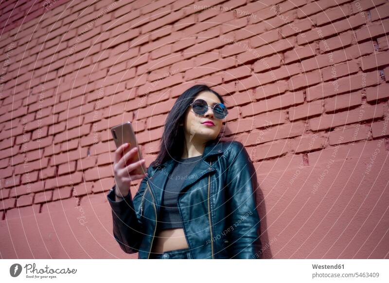 Portrait of young woman with smartphone wearing sunglasses and black leather jacket Smartphone iPhone Smartphones sun glasses Pair Of Sunglasses portrait