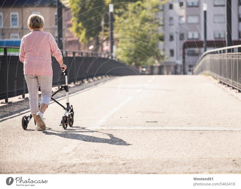 Senior woman with wheeled walker on footbridge jumper sweater Sweaters go going hold colour colours Rosy Social Issue Social Theme Social Themes Social Topic