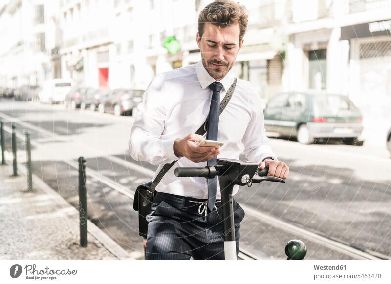 Young businessman with e-scooter using mobile phone in the city, Lisbon, Portugal business life business world business person businesspeople Business man