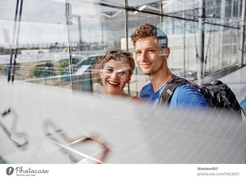 Portrait of smiling couple at the airport looking out of window portrait portraits view seeing viewing smile windows twosomes partnership couples terminal