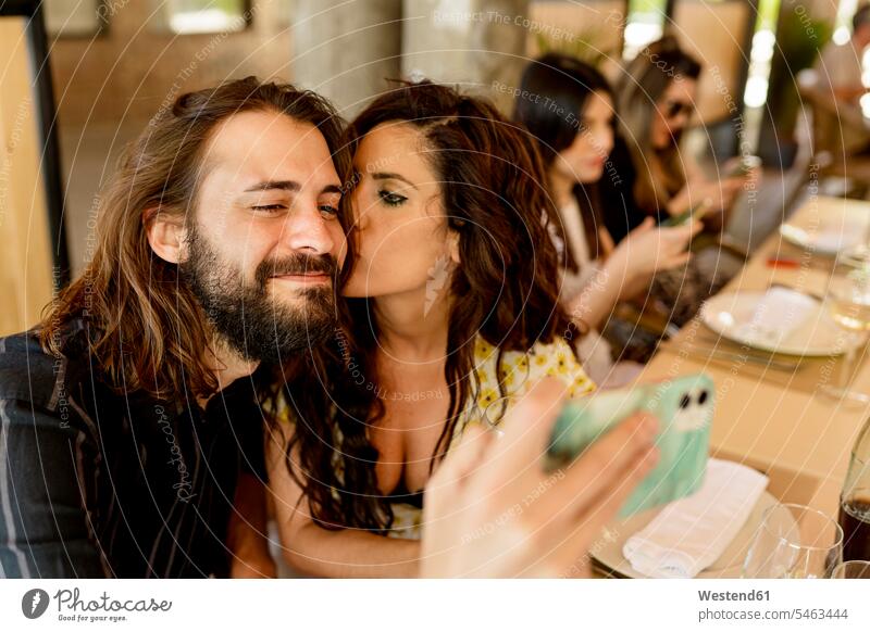 Man taking selfie while woman kissing him at restaurant color image colour image Spain indoors indoor shot indoor shots interior interior view Interiors day