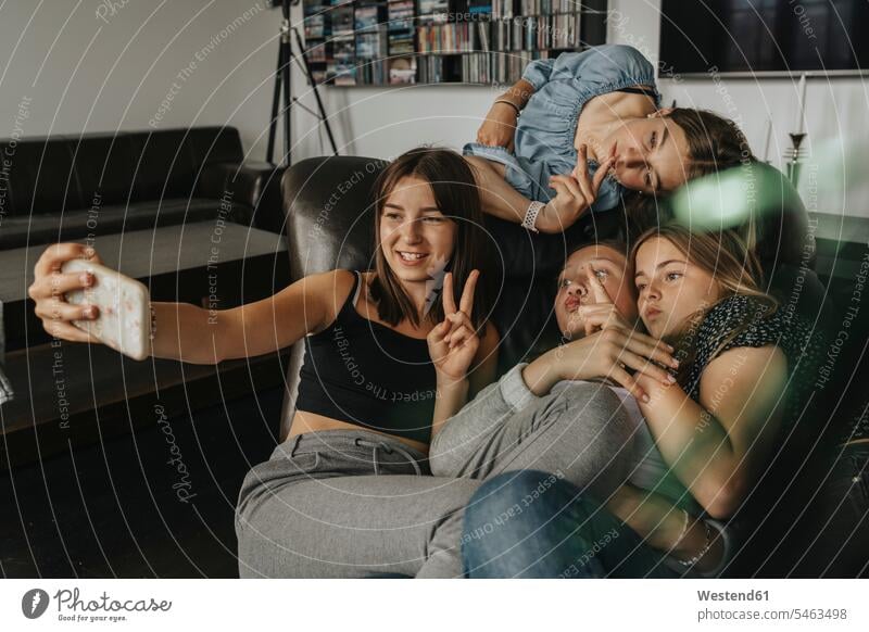 Friends gesturing while taking selfie on sofa at home color image colour image Germany indoors indoor shot indoor shots interior interior view Interiors