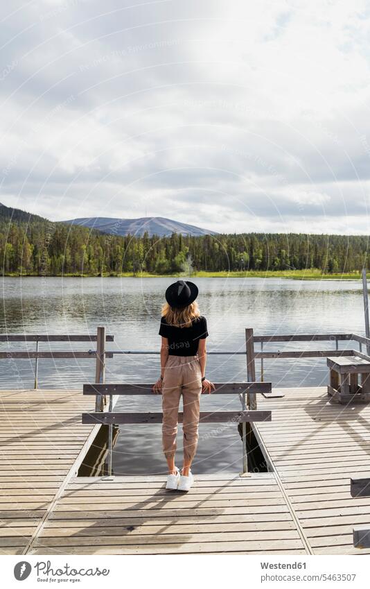 Finland, Lapland, woman wearing a hat standing on jetty at a lake hats lakes jetties females women water waters body of water Adults grown-ups grownups adult