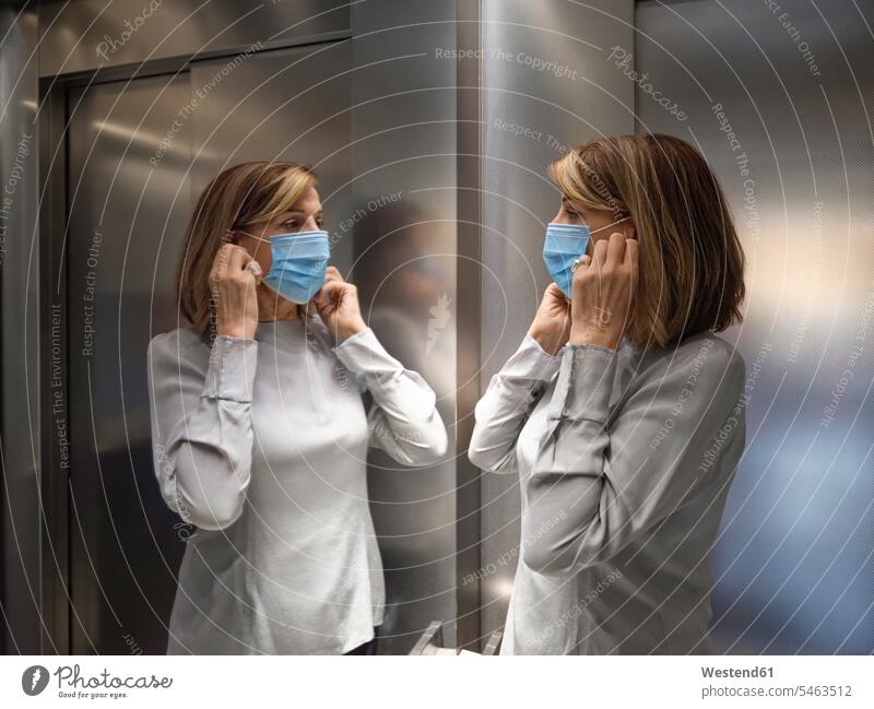 Senior woman wearing protective face mask while standing in elevator during covid-19 color image colour image indoors indoor shot indoor shots interior