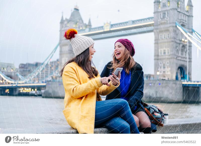 London, United Kingdom, Girlfriends sitting on railing in front of Tower Bridge image picture pictures images photograph photos photographs horizontal