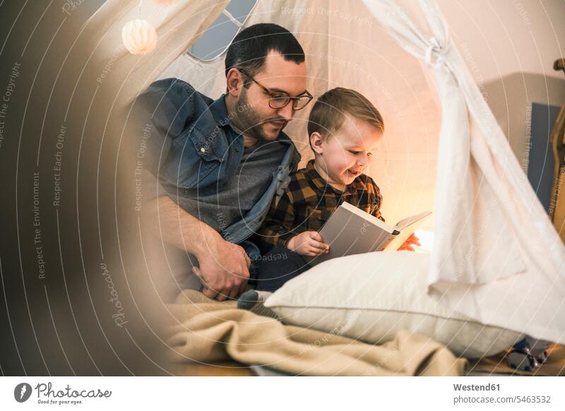 Father and son reading a book together in tent at home books tents sons manchild manchildren father pa fathers daddy dads papa family families people persons