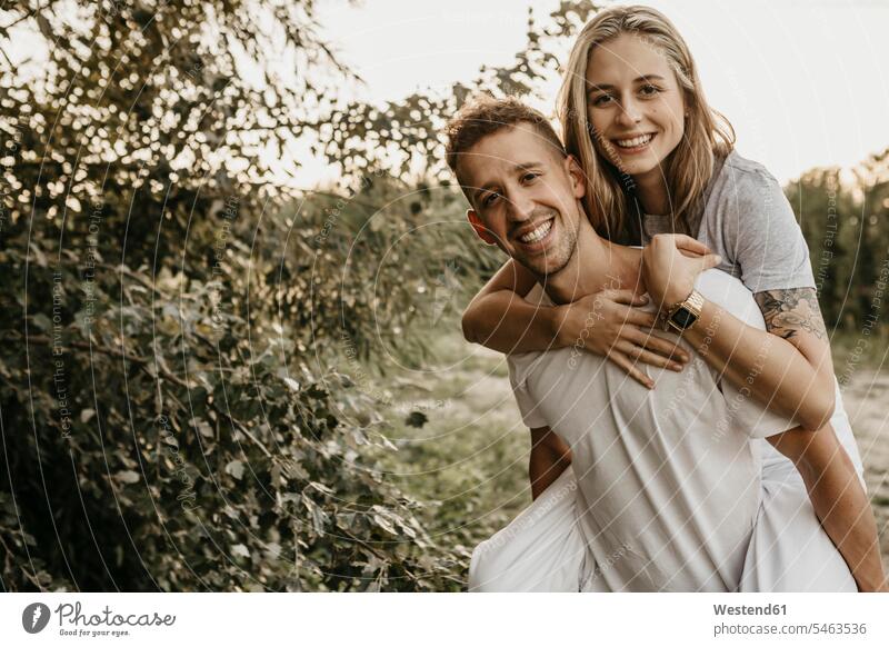 Portrait of young smiling couple, man carrying woman on back T- Shirt t-shirts tee-shirt hold embrace Embracement hug hugging in the evening delight enjoyment