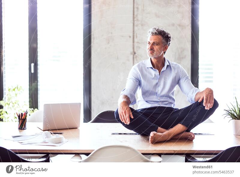 Mature businessman sitting barefoot on desk in office Seated desks offices office room office rooms naked feet naked foot Barefeet Bare Feet Bare Foot