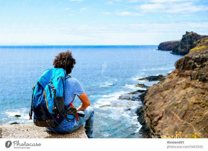 Spain, Canary Islands, Gran Canaria, Man with backpack sitting on cliff tourist tourists View Vista Look-Out outlook Traveller Travellers Travelers man men