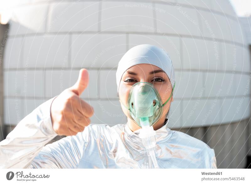 Woman wearing protective suit and oxygen mask showing thumbs up while standing against igloo color image colour image outdoors location shots outdoor shot
