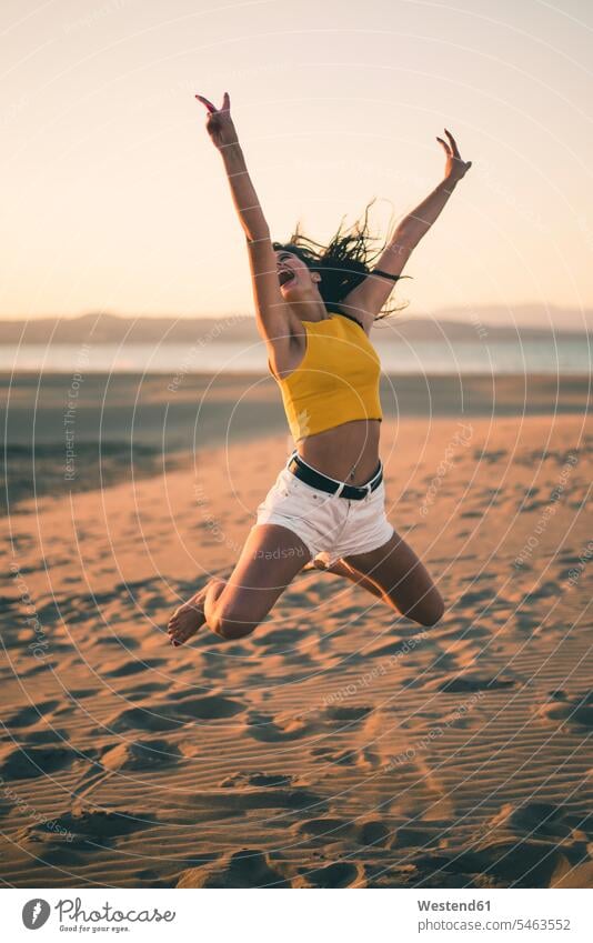 Happy teenage girl jumping in the air on the beach at sunset beaches sunsets sundown Teenage Girls female teenagers happiness happy Leaping jump in the air