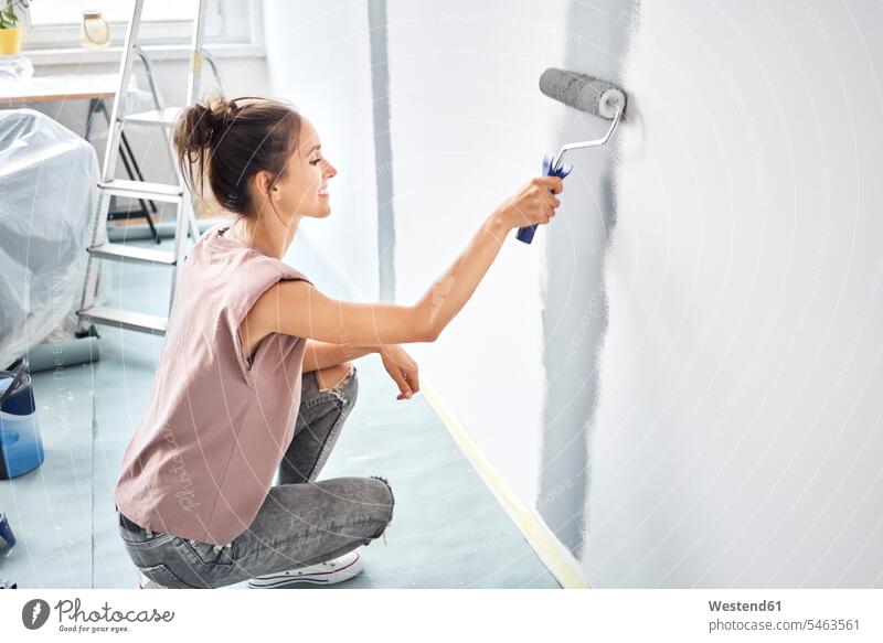 Smiling woman painting with paint roller on wall while crouching at home color image colour image indoors indoor shot indoor shots interior interior view