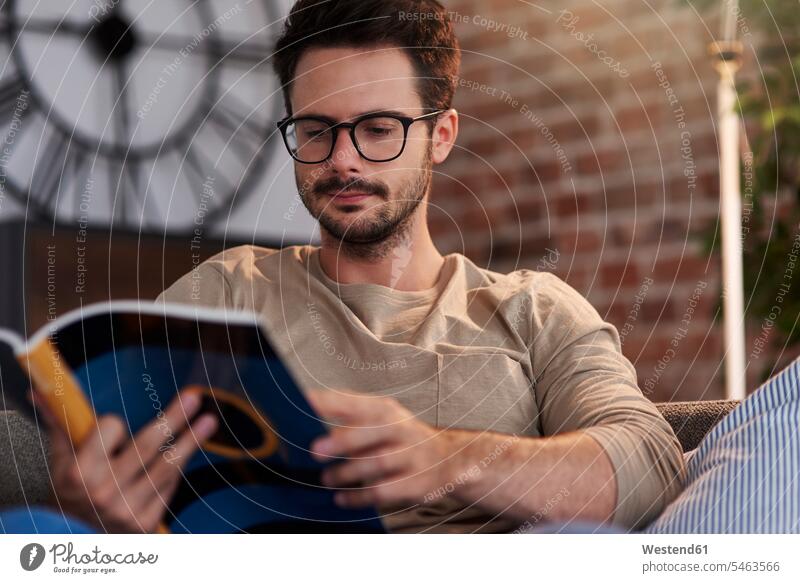 Portrait of man sitting on couch at home reading a book Seated settee sofa sofas couches settees men males books portrait portraits Adults grown-ups grownups