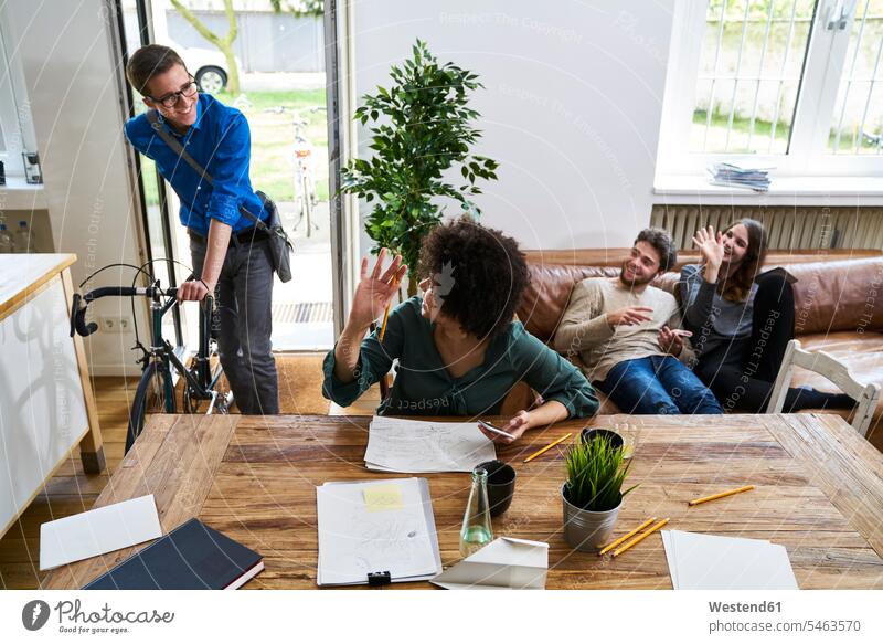 Coworkers waving at young man with bicycle arriving in modern office Arrival arrive bikes bicycles offices office room office rooms contemporary wave workplace
