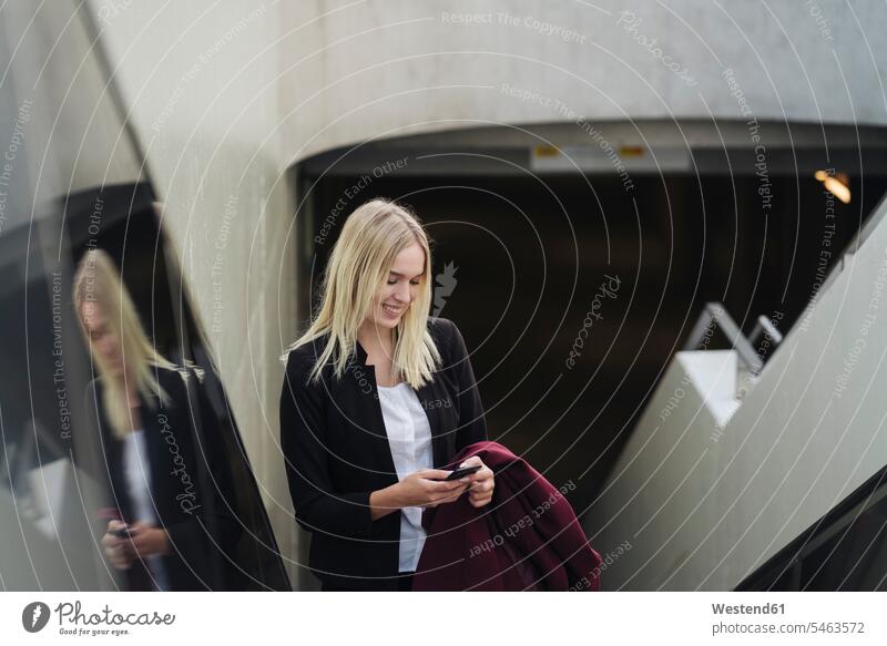 Blond businesswoman using smartphone while using escalator human human being human beings humans person persons caucasian appearance caucasian ethnicity
