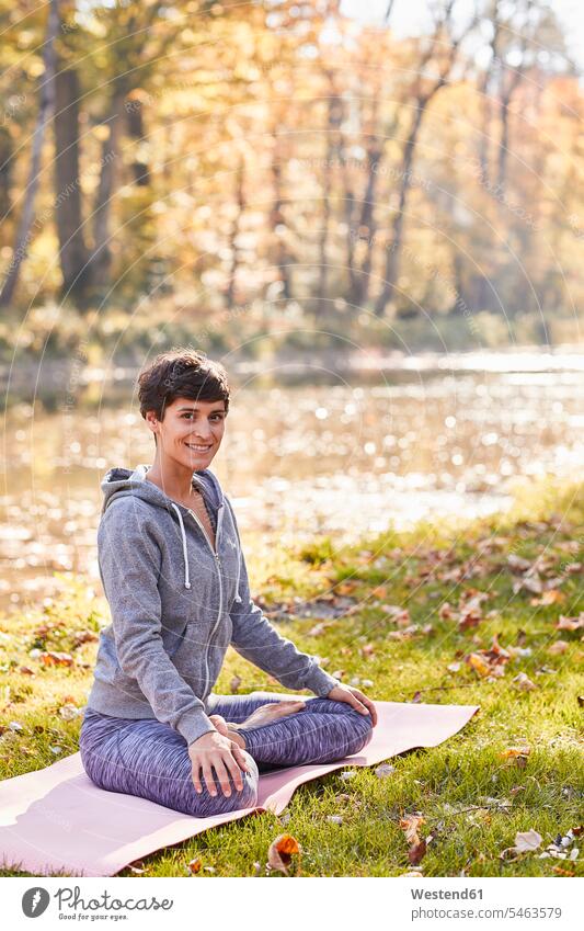 Smiling mid adult woman in forest practicing yoga, lotus position females women woods forests sitting Seated smiling smile Adults grown-ups grownups people