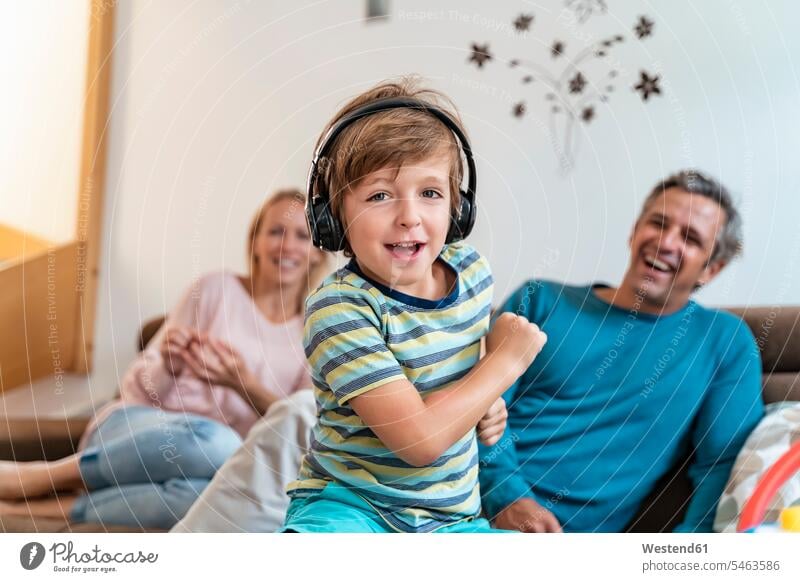 Portrait of boy listening to music with headphones on couch at home with parents in background couches settee settees sofa sofas headset hear play Ardor Ardour