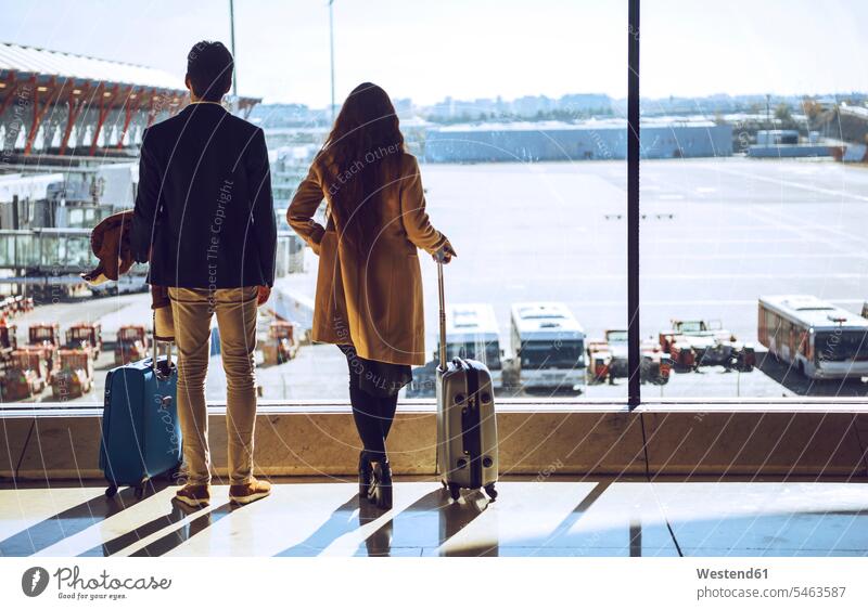 Business couple looking through window at airport departure area color image colour image indoors indoor shot indoor shots interior interior view Interiors day