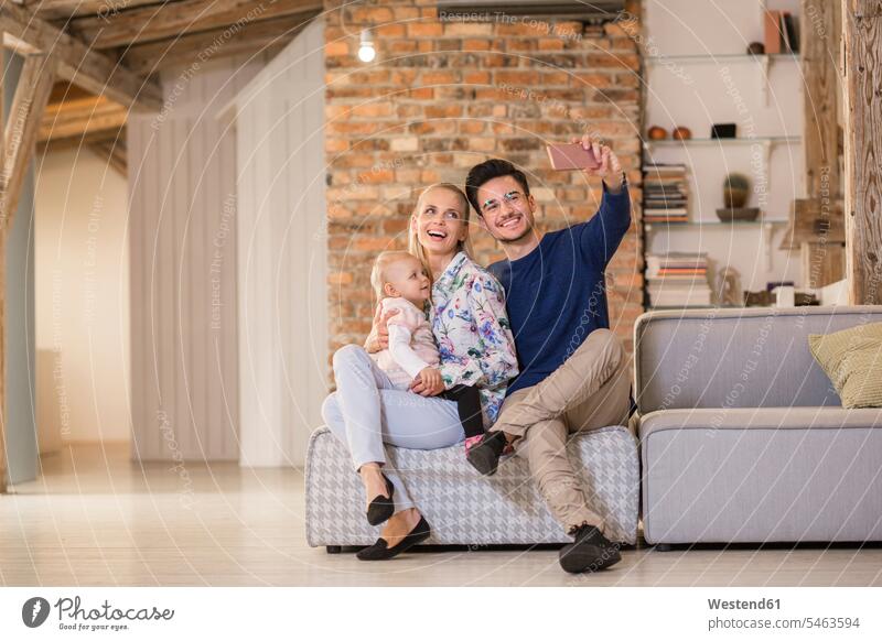 Happy young parents taking a selfie on couch at home with their baby girl settee sofa sofas couches settees happiness happy Selfie Selfies family families