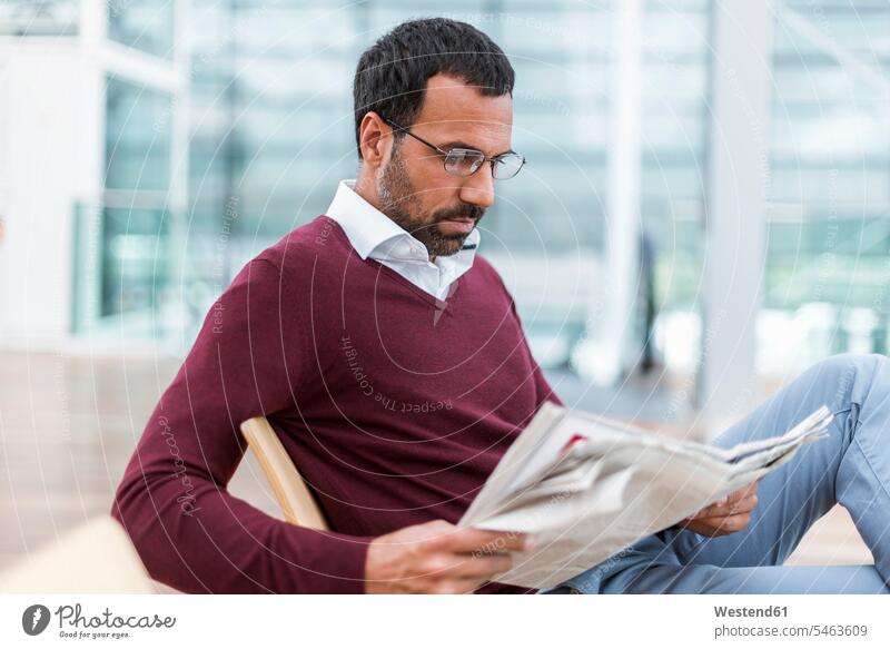Businessman reading a newspaper in waiting hall men males newspapers glasses specs Eye Glasses spectacles Eyeglasses Business man Businessmen Business men