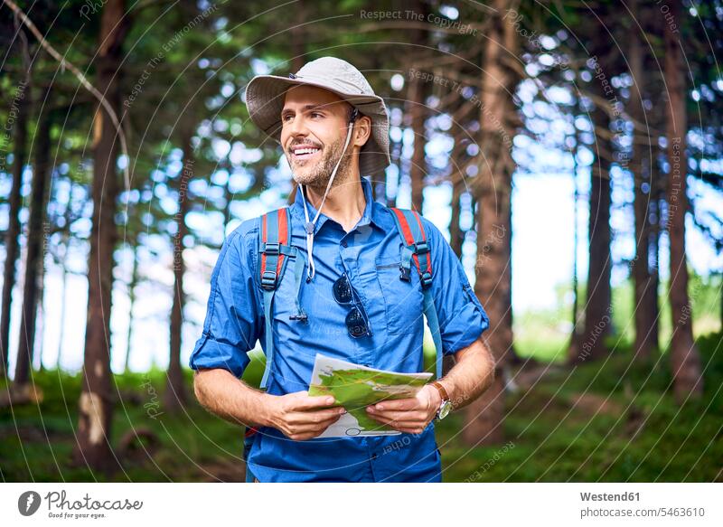 Smiling man holding a map hiking in the forest woods forests men males hike smiling smile maps Adults grown-ups grownups adult people persons human being humans