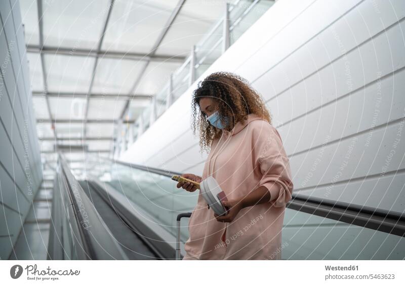 Young woman using smart phone while standing on escalator at airport color image colour image indoors indoor shot indoor shots interior interior view Interiors