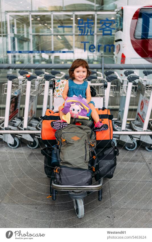 Baby girl sitting on the top of the luggage in a trolley at the airport terminal airports Departure departing leaving globetrotter smiling smile baggage cart