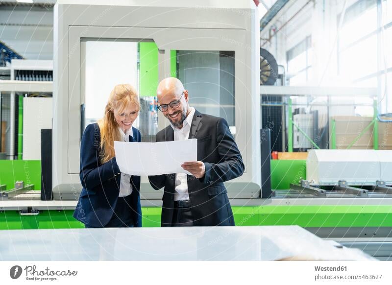 Smiling businessman and businesswoman looking at plan in factory plans smiling smile Businessman Business man Businessmen Business men businesswomen