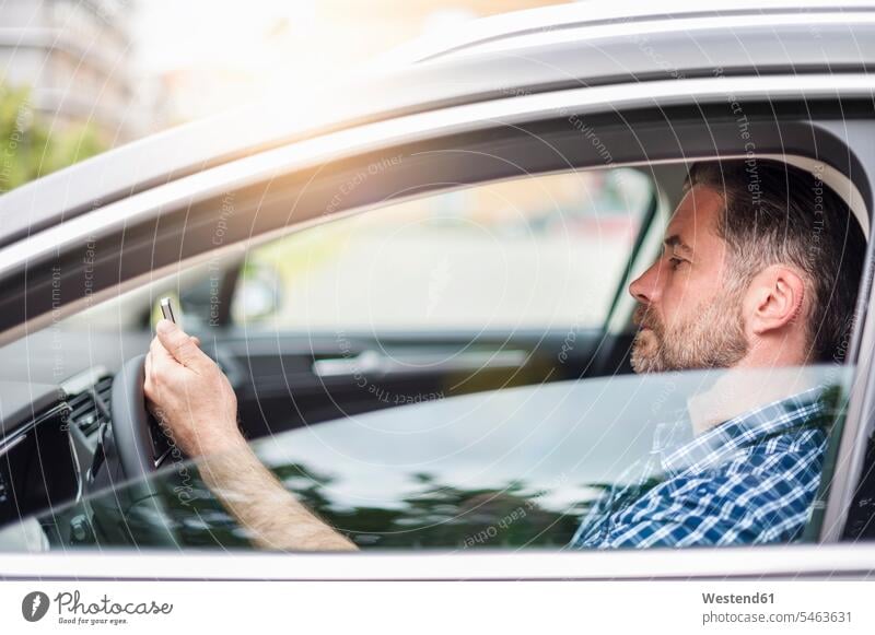 Side view of handsome man using mobile phone while sitting in car color image colour image Germany outdoors location shots outdoor shot outdoor shots day