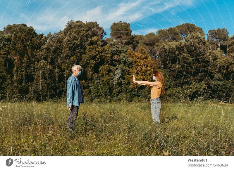 Woman and senior man with masks standing on meadow, holding safety distance reclusive reclusively risky protect protecting Safety secure on the go on the road
