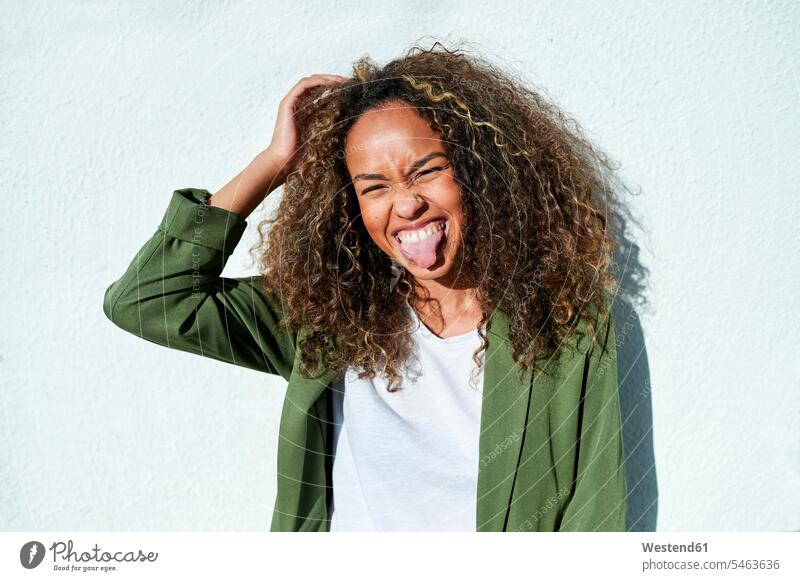 Playful woman sticking out tongue against white wall during sunny day color image colour image outdoors location shots outdoor shot outdoor shots daylight shot