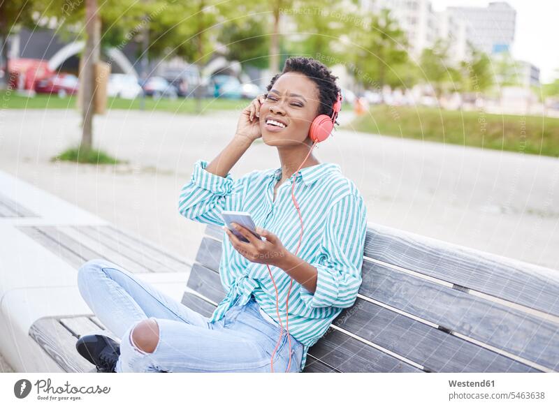 Portrait of young woman sitting on bench listening music with cell phone and headphones benches hearing portrait portraits Smartphone iPhone Smartphones females
